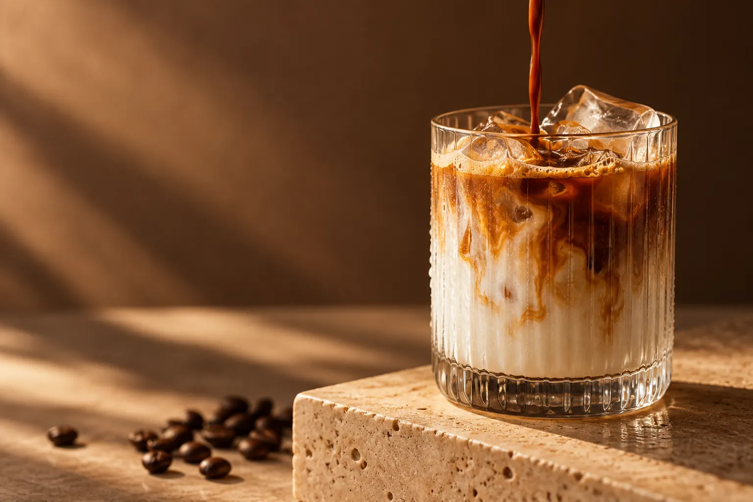 Espresso poured over milk and ice in a glass on warm travertine